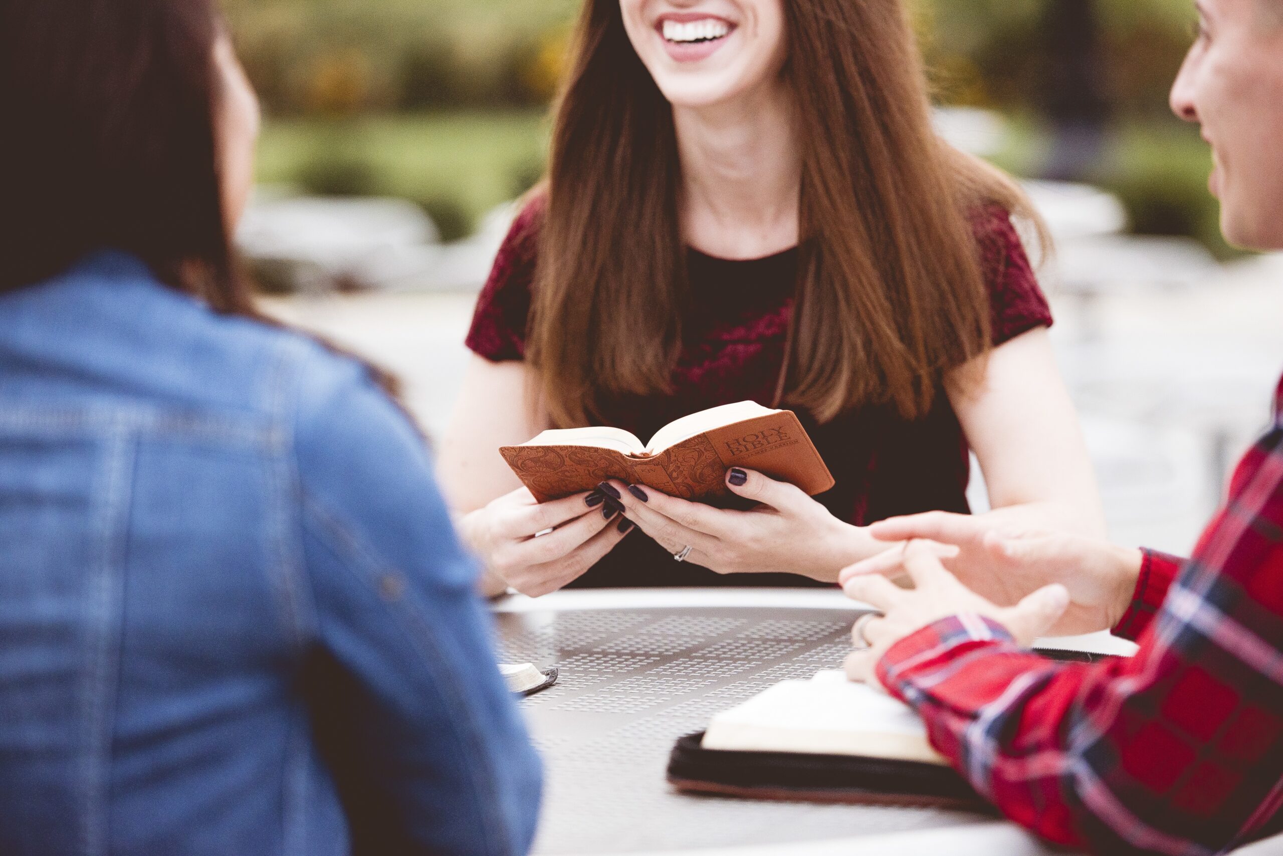 Closeup shot of females sitting around a table and reading the holy bible with a blurred background A closeup shot of females sitting around a table and reading the holy bible with a blurred background